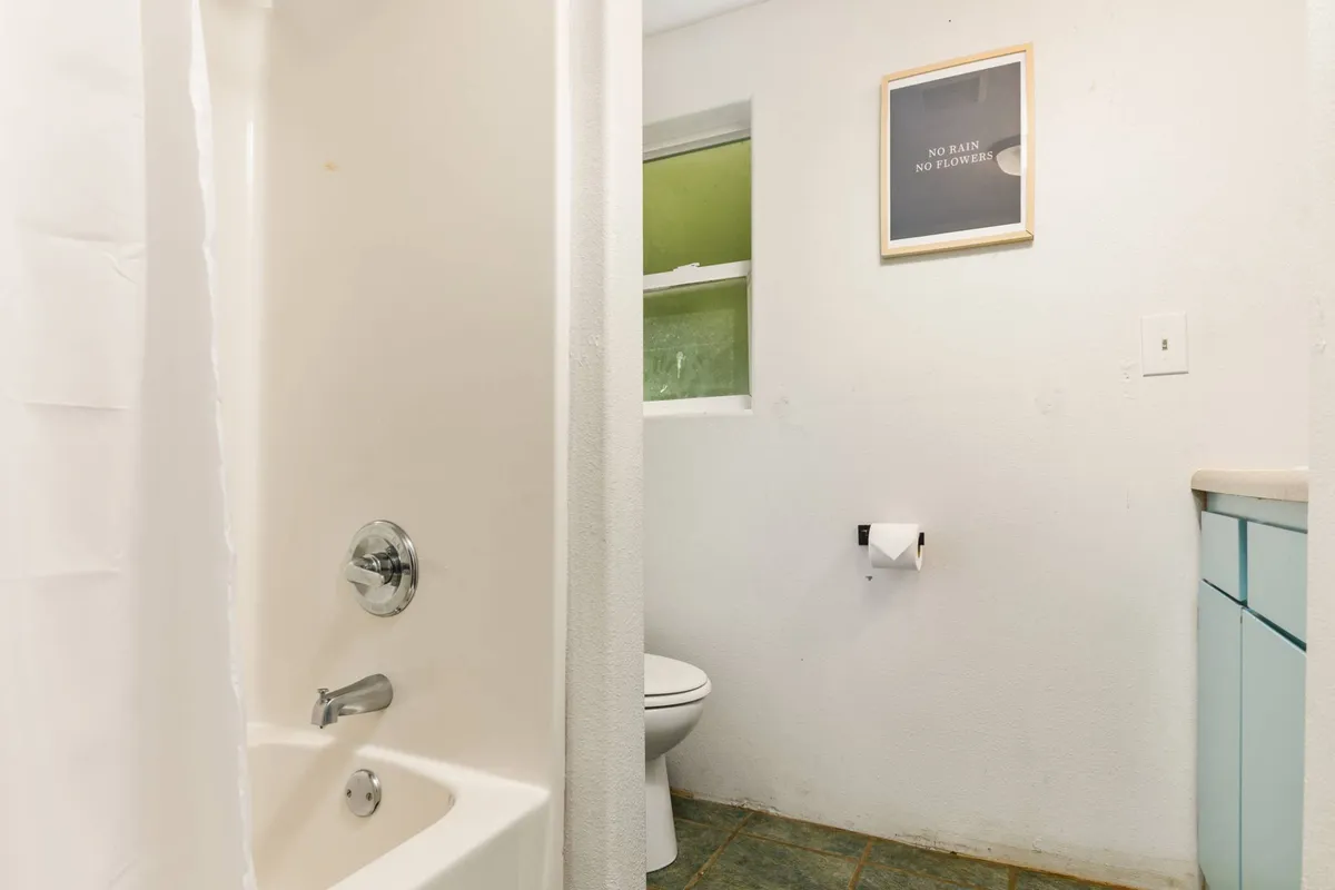 This image displays the bathroom's shower area, toilet, a framed artwork on the wall, and a vanity unit. The space is bright and airy, with natural light highlighting the clean surfaces and practical layout. The overall look is uncluttered and inviting, suggesting both functionality and tranquility.