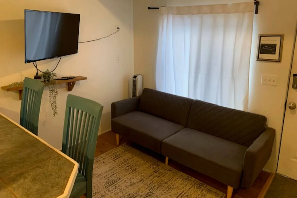 This image displays a cozy living area featuring a comfortable sofa, television, and a dining space. The layout suggests a welcoming common area where guests can unwind, socialize, or spend quiet moments together. The visible open space is ideal for relaxing with a pet after a day out exploring the coast.