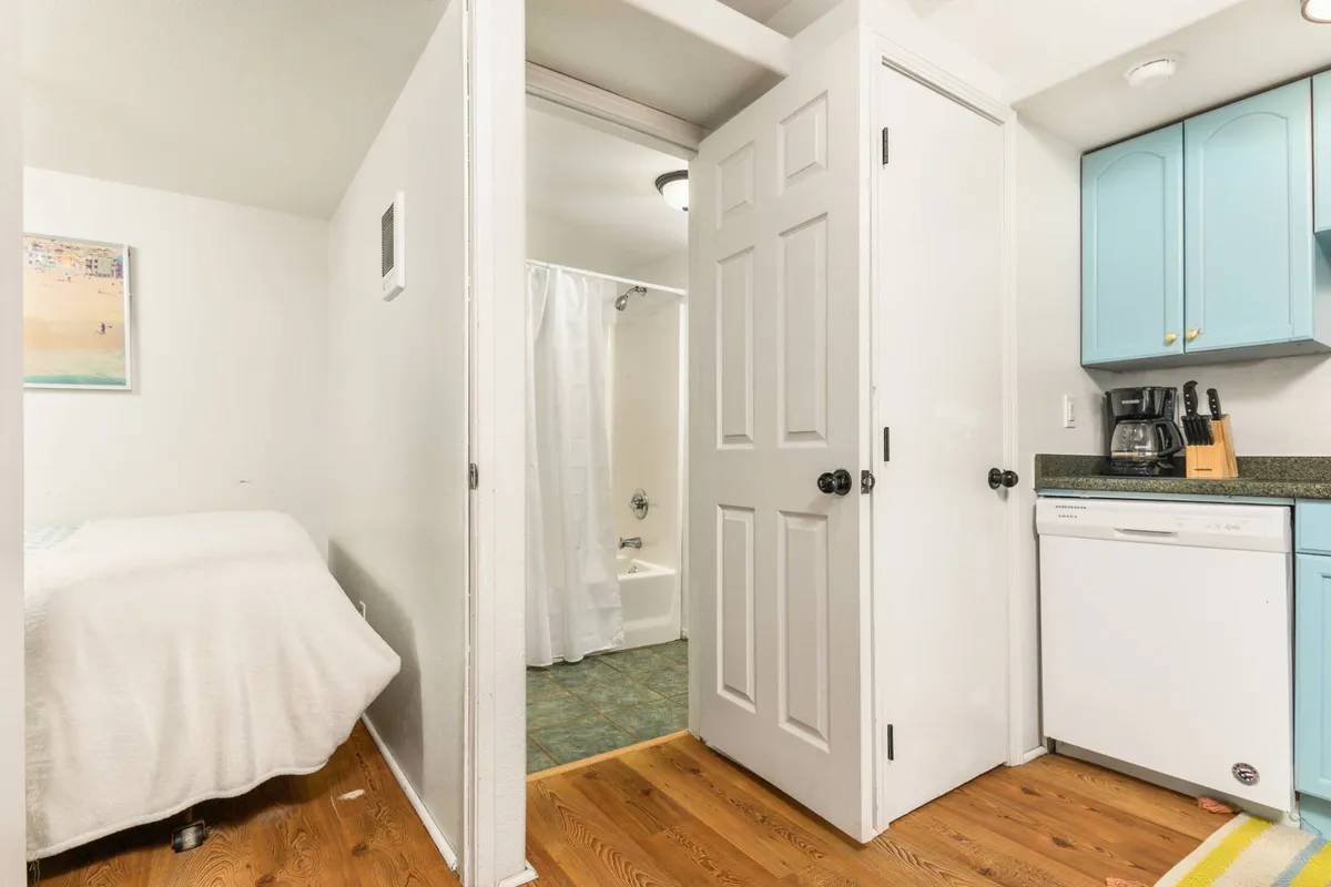 This interior shot highlights a comfortable bed adjacent to a compact kitchenette and the door to the bathroom. The space feels functional yet cozy, perfect for solo travelers or couples. The lighting and arrangement suggest warmth and convenience in a compact footprint.