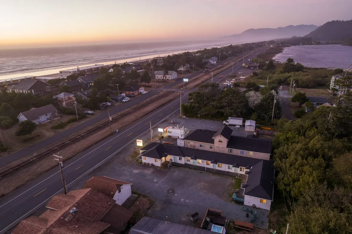This image showcases the ocean view from the motel, with the foreground including a roadway, surrounding houses, and a visible parking area. The atmosphere is serene, connecting the property directly to its coastal location and inviting guests to imagine outdoor experiences near the sea.
