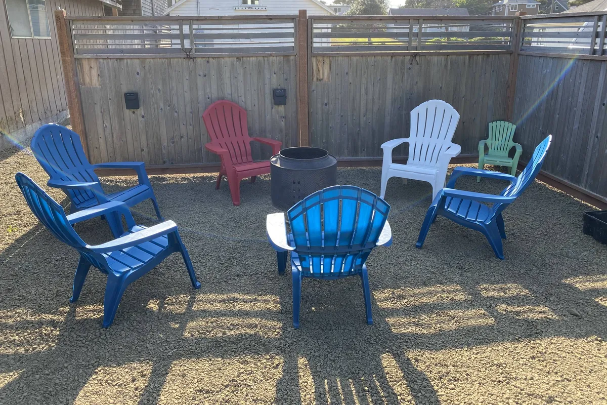 A relaxed outdoor setting featuring colorful Adirondack chairs arranged around a central fire-pit, bordered by a wooden fence. The ambiance suggests an ideal spot for guests to gather, socialize, and enjoy the evening sky together.